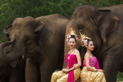 Females in traditional clothing sitting by elephants