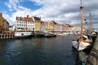 Sailboats moored on river by buildings in city against sky