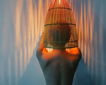 Close-up of hand holding illuminated lamp against wall