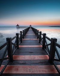Empty pier over sea against sky during sunset