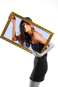 Digital composite image of young woman holding picture frame while standing against white background