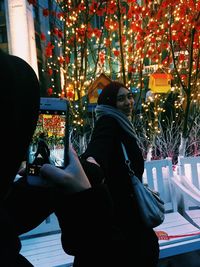 Rear view of woman photographing illuminated city in park