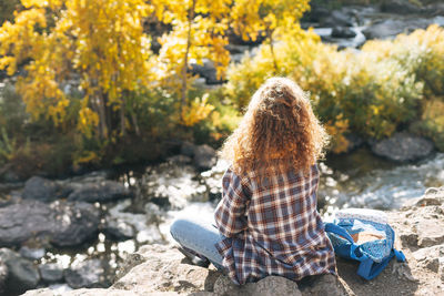 Young woman with curly hair in plaid shirt, jeans looks at magic view of mountains and river