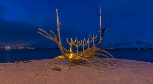 Dead tree on beach against blue sky at night