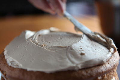 Cropped hand spreading cream on cake