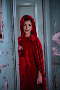 Portrait of young woman standing against red wall