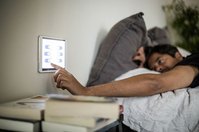 Man using digital tablet mounted on wall while lying on bed at smart home