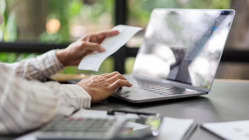 Business concept, businesswoman holds receipt to checking expense of project and typing on laptop.