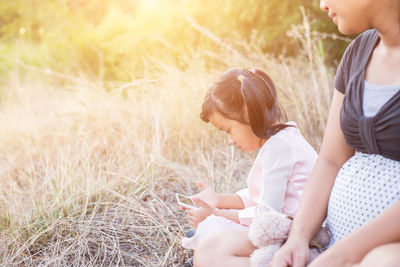 Side view of mother and girl sitting on plant