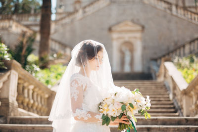 Bride holding bouquet standing outdoors