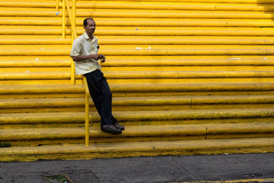 Full length of man leaning on railing at yellow steps