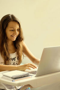 Businesswoman using laptop at desk against white wall