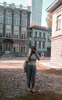 Full length of woman standing on street against buildings in city