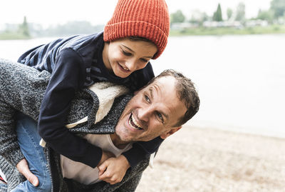 Happy father carrying son on piggyback at the riverside