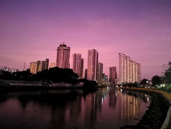 River by illuminated buildings against sky at sunset