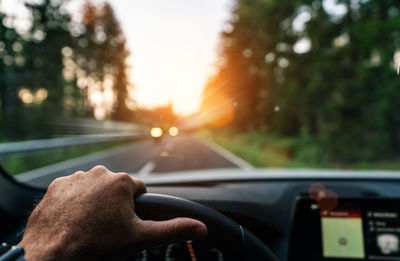Cropped hand of man driving car during sunset