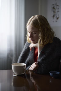 Pensive teenage girl sitting at table with cup of tea