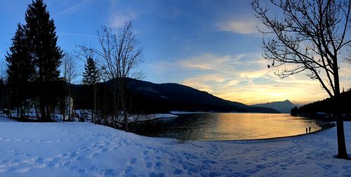 Scenic view of lake by snowcapped mountains against sky at sunset