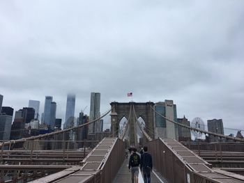 People walking on bridge against sky in city