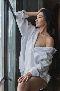 Side view of young woman looking through window