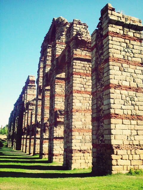 architecture, built structure, building exterior, clear sky, grass, brick wall, blue, low angle view, old, sunlight, wall - building feature, stone wall, sky, day, outdoors, no people, history, building, window, shadow