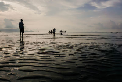 Silhouette people on beach against sky during sunset