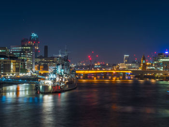 Illuminated buildings by sea against sky at night