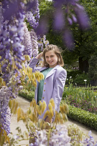 A young woman in a lilac jacket poses near the flowering wisteria in the garden