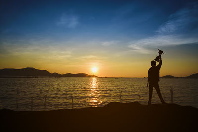 Silhouette person standing at beach against sky during sunset