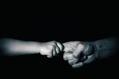 Cropped image of people holding hands over black background