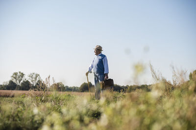 Senior man carrying traveling bag, walking in the fields