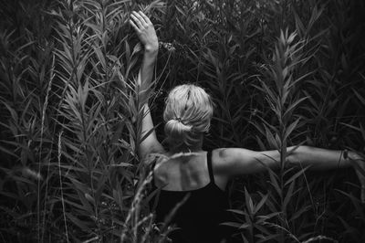 Rear view of woman with arms raised amidst plants