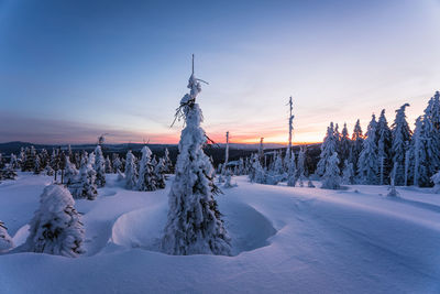 Snow covered landscape against sky during sunset