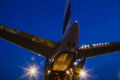 Low angle view of illuminated airplane against clear blue sky