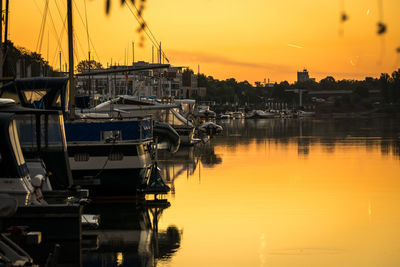 Boats moored in harbor at sunset