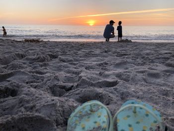 People standing on beach against sky during sunset