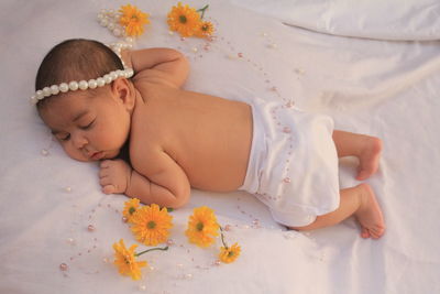 Close-up of baby girl with flowers on bed