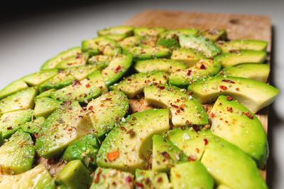 Large slices of sliced ripe avocado lie textured on a wooden cutting board. sprinkled with spices