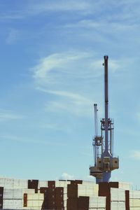 Low angle view of containers and crane at commercial dock against sky