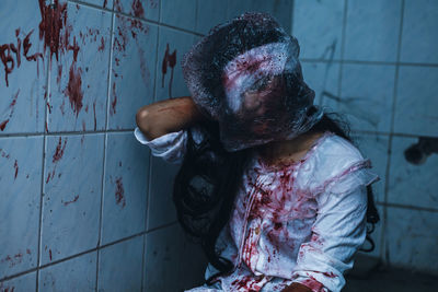 Woman with spooky make-up sitting by wall