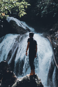 Full length of man standing on rock against waterfall