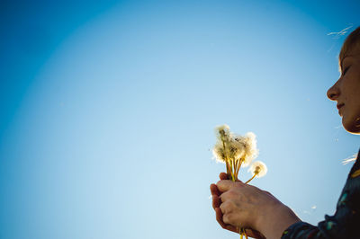 Woman holding dandelion while standing against sky