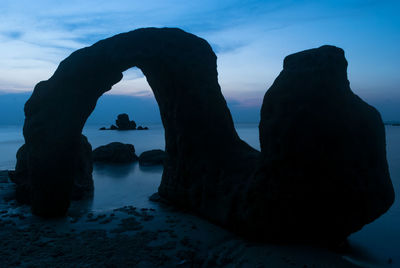 Silhouette rocks on sea shore against sky