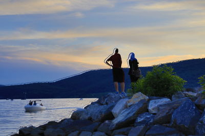 People on rock by sea against sky during sunset