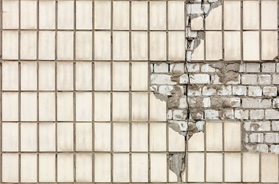 A crack on the wall of a brick house with a fallen off rectangular facade tile.