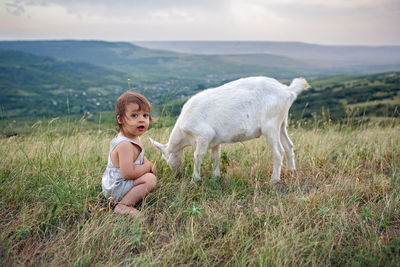 Baby boy playing in the field with a small goat