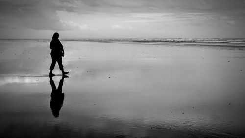 Silhouette woman standing on wet beach