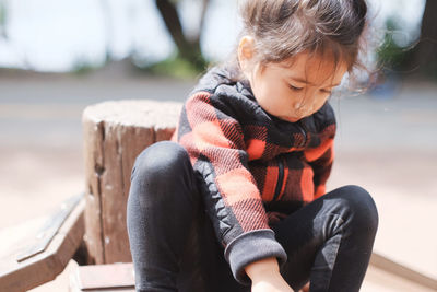 Cute little girl sitting on wood on sunny day