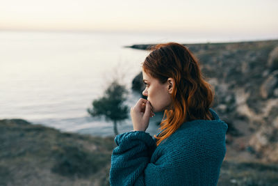 Young woman standing by sea against sky during sunset