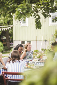 Family and friends enjoying food while sitting together at table in backyard